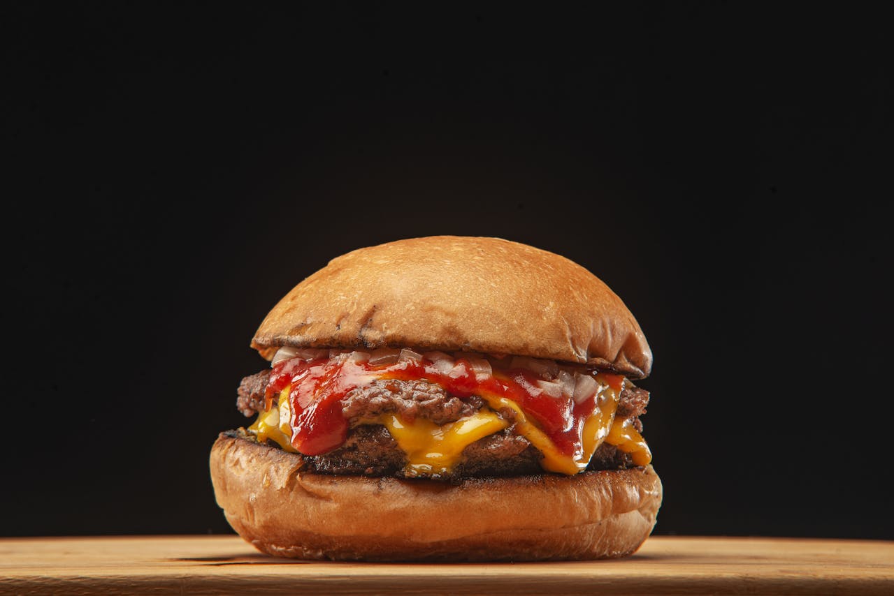 A classic cheeseburger with melted cheddar, a generous drizzle of ketchup, and finely diced raw onion on a toasted bun.