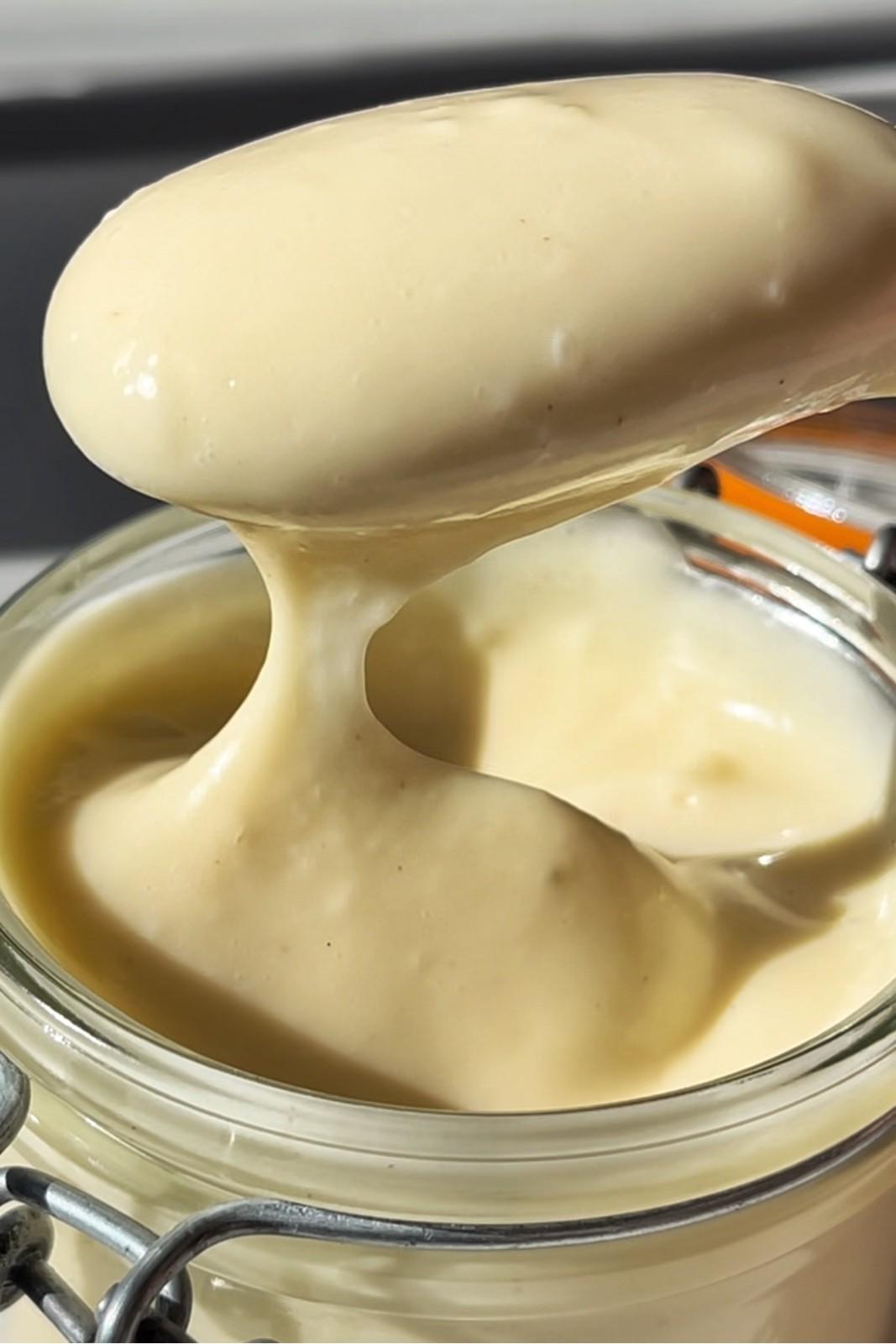 A spoon with a dollop of mayonnaise from a kilner jar full of mayonnaise, a great burger topping sauce.