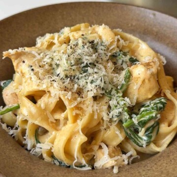 Chicken spinach alfredo in a brown bowl garnished with parmesan.