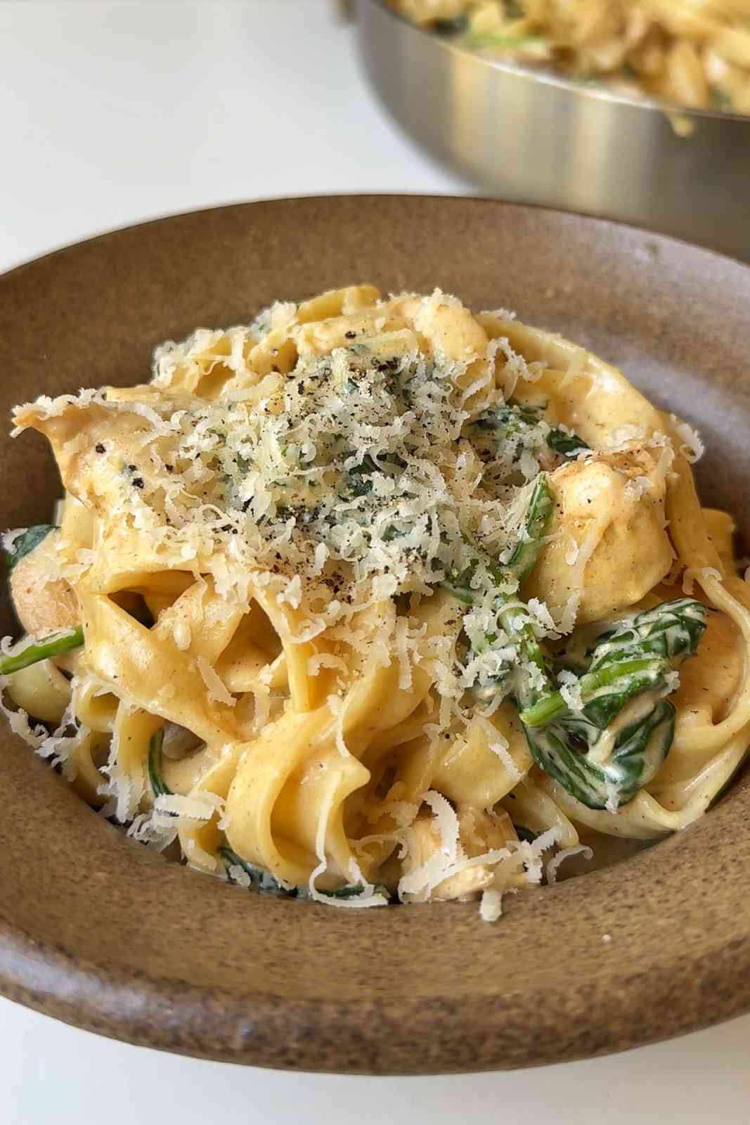 Chicken spinach alfredo in a brown bowl garnished with parmesan.