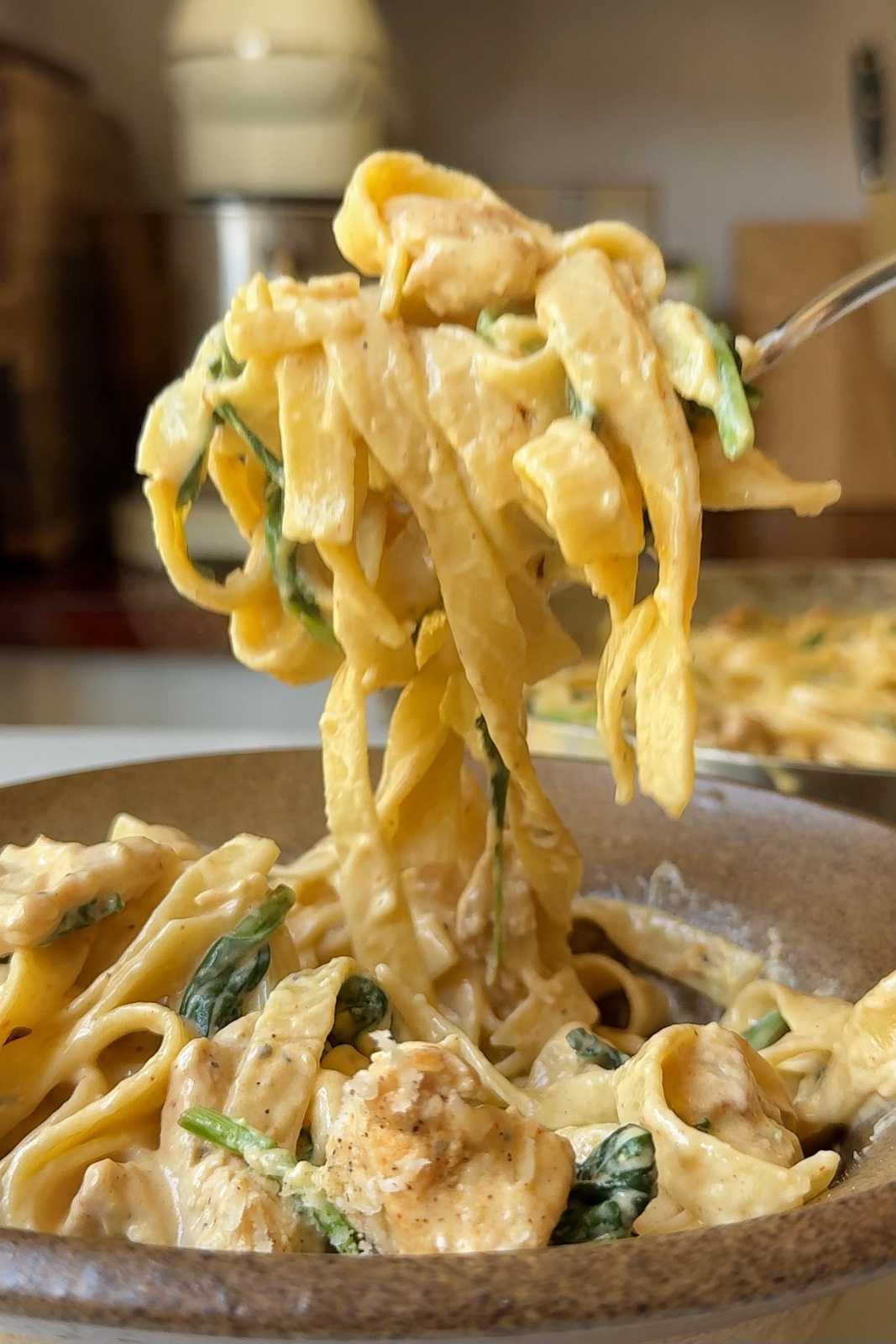 Forkful of chicken spinach alfredo pasta.