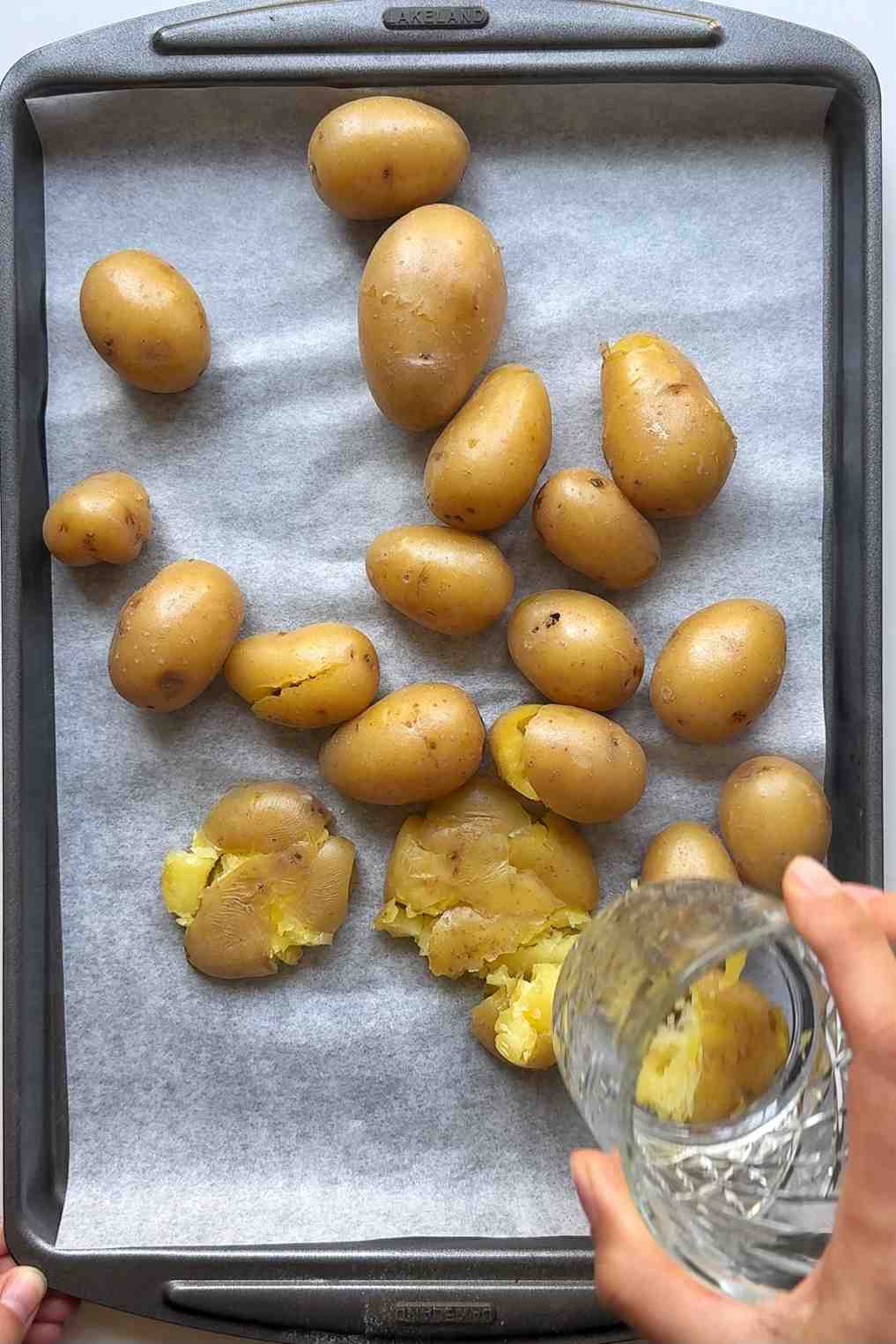 Smashing potatoes using a glass on a tray with parchment paper.