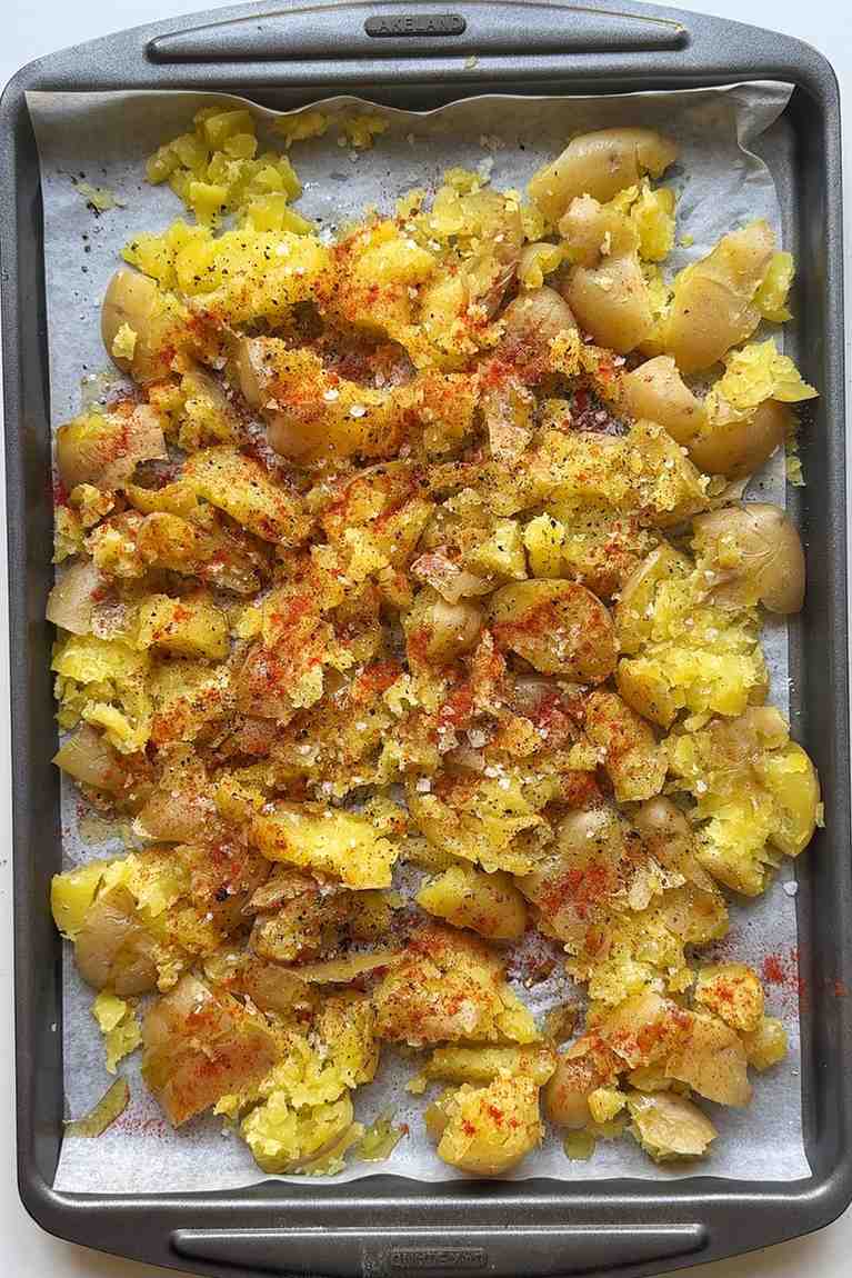 Seasoning the smashed potatoes on a tray.