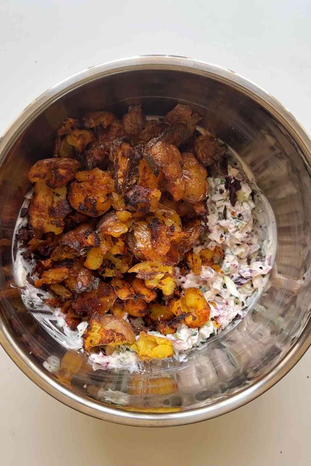 Adding crispy roasted potatoes into the salad dressing to toss.