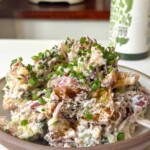 Crispy smashed potato salad topped with chives in a brown bowl on a white background.