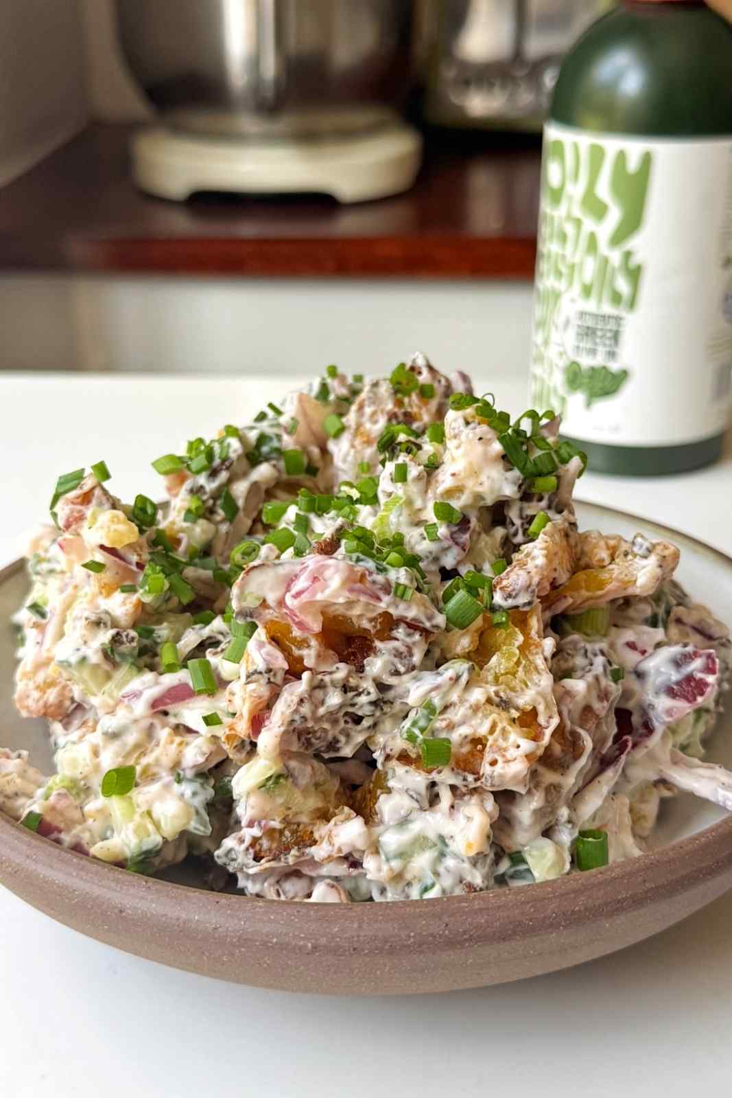 Crispy smashed potato salad topped with chives in a brown bowl on a white background.
