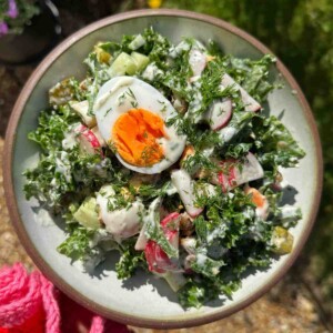 A bowl of fresh dill salad with kale, radish, cucumber, and a soft-boiled egg, topped with generous sprigs of fresh dill and a creamy dressing, held in hand on a sunny day outdoors.