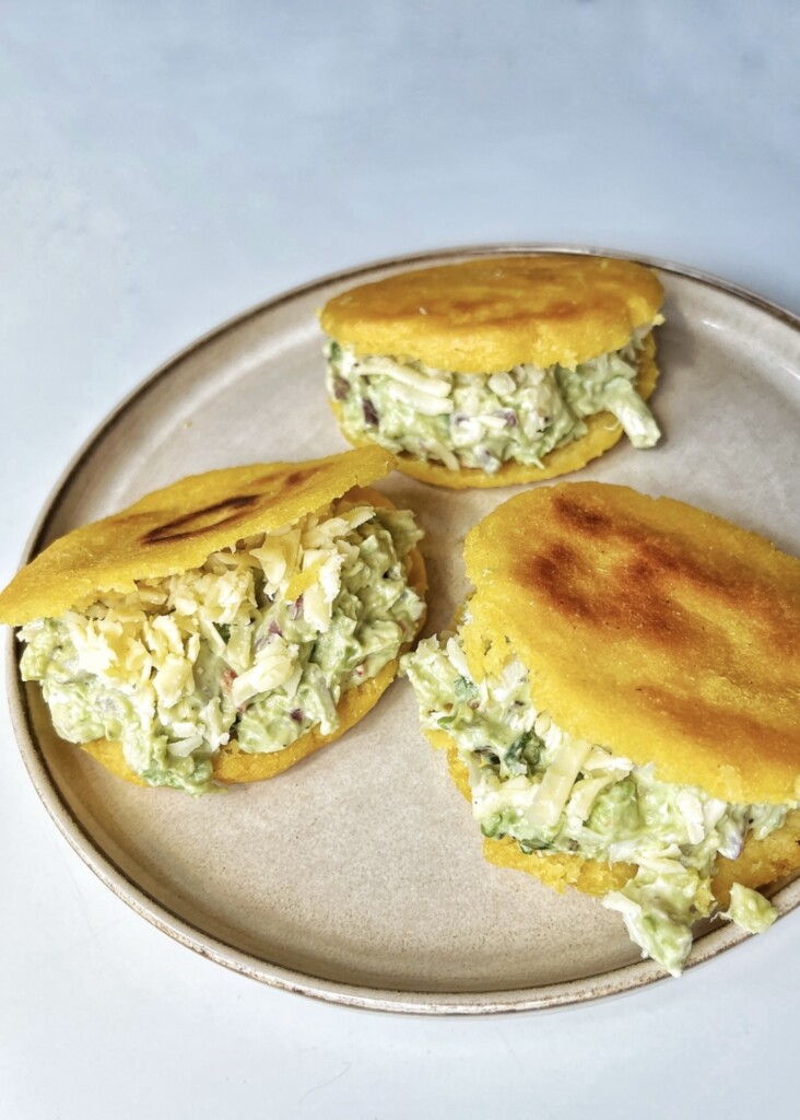 Three golden Venezuelan arepas reina pepiada on a plate stuffed with chicken and avocado salad.