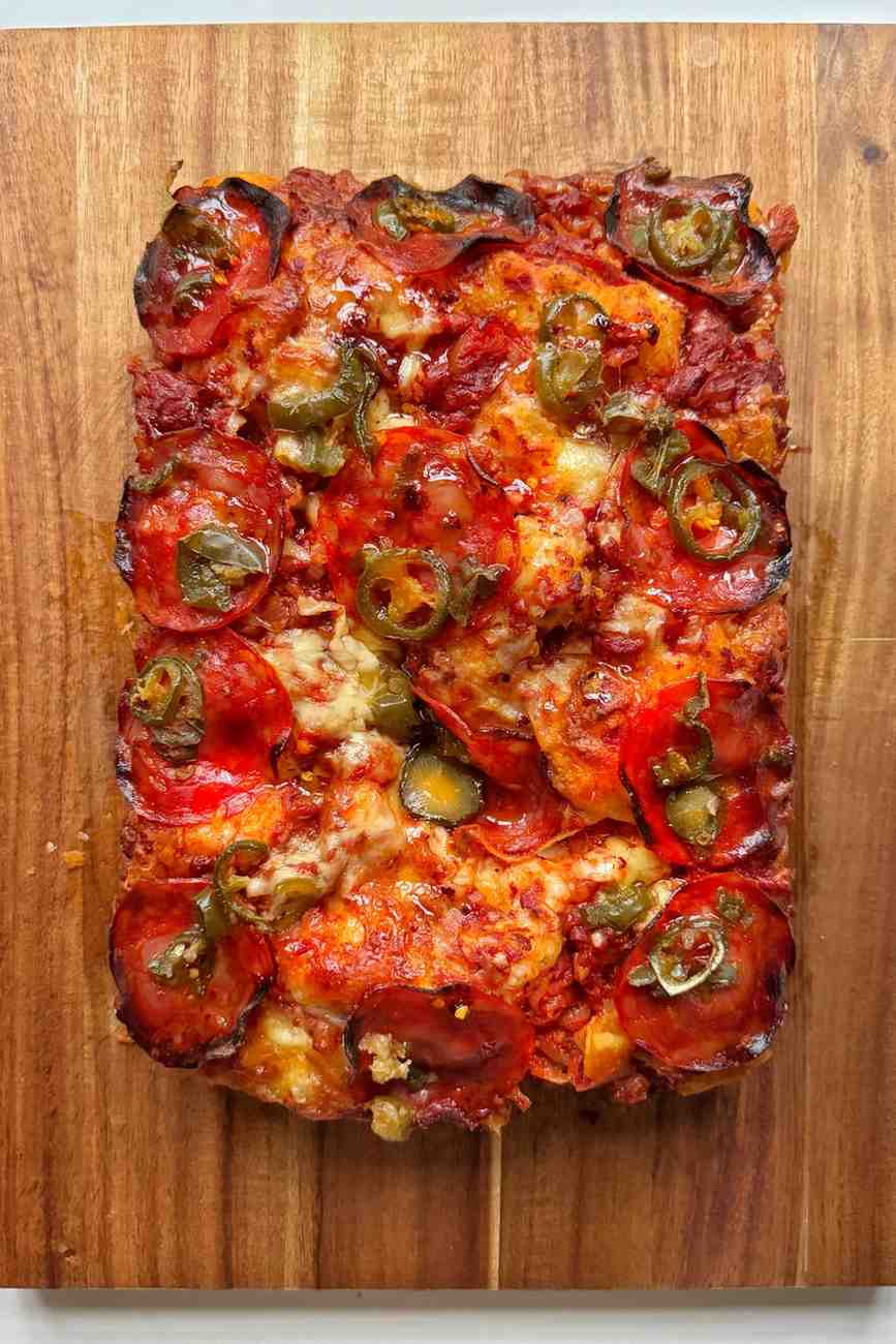 Pepperoni and hot honey pizza focaccia with jalapeños and melted cheese seen from above on a wooden board.