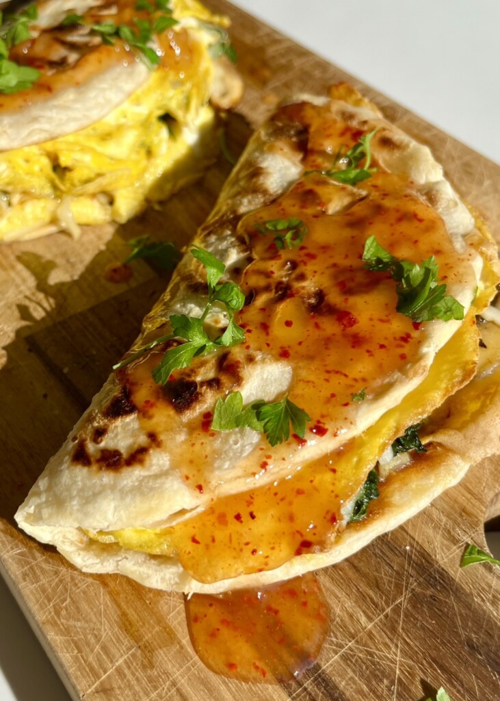 Breakfast paratha folded with egg and drizzled with chili sauce and fresh herbs on a wooden board.