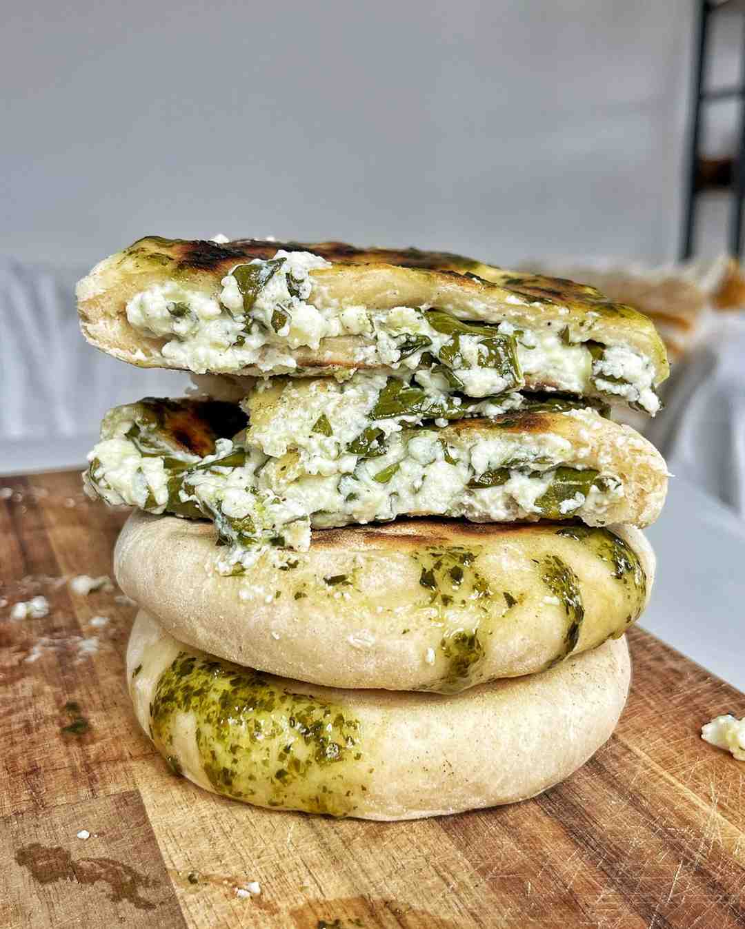 Feta spring flatbreads stacked on a wooden board with the top one sliced open to reveal feta spinach and mint filling.