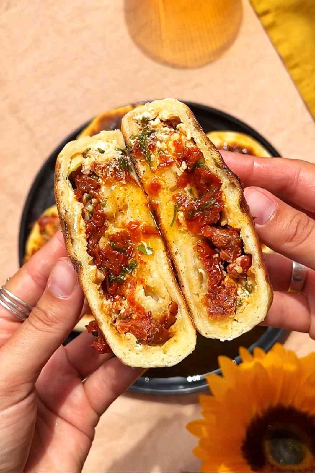 Hands holding a caprese stuffed flatbread cut in half showing sun-dried tomato feta and mozzarella filling with basil.