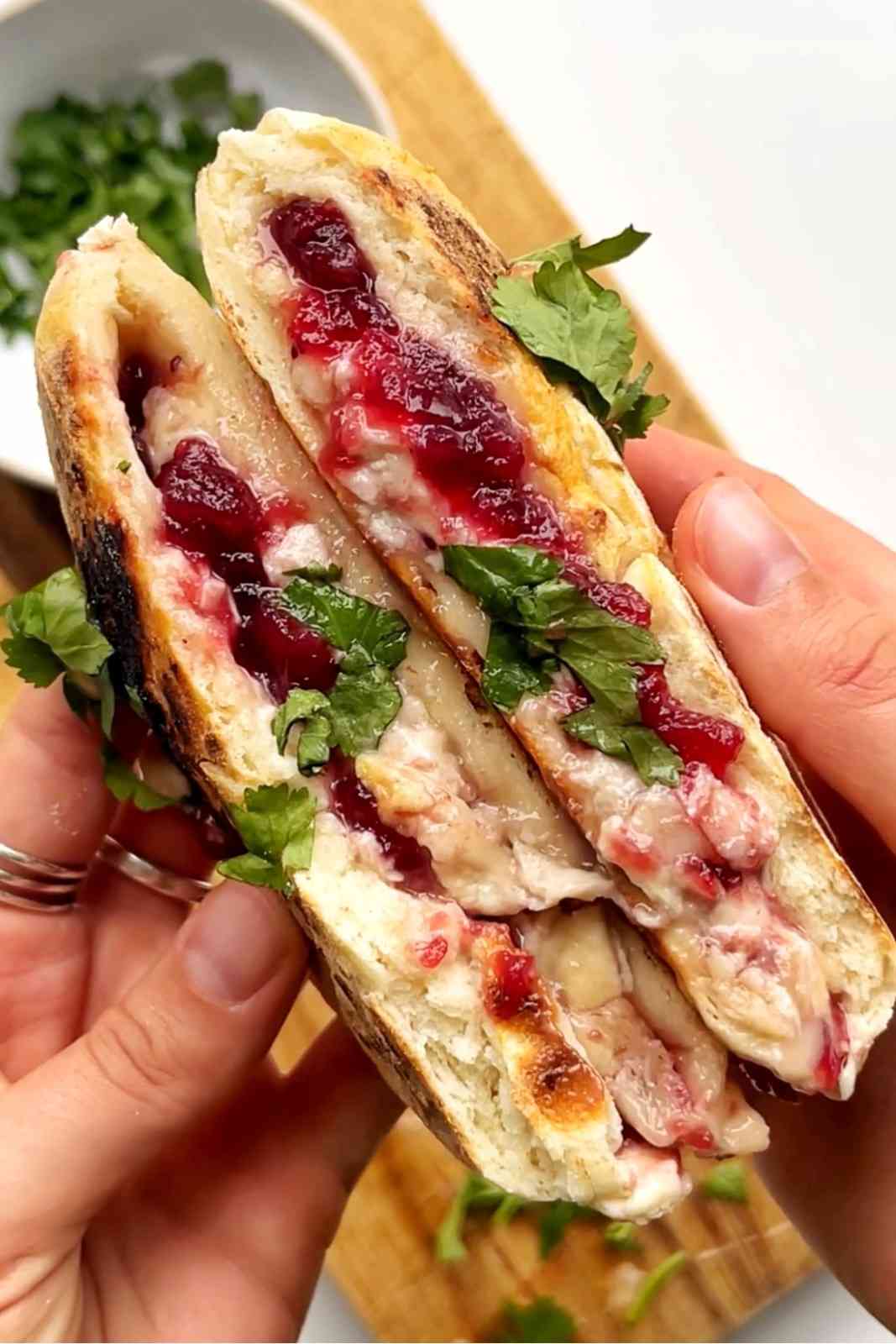 Festive turkey flatbreads held in hand showing melted brie and cranberry sauce filling with fresh herbs, one of the best flatbread recipes.