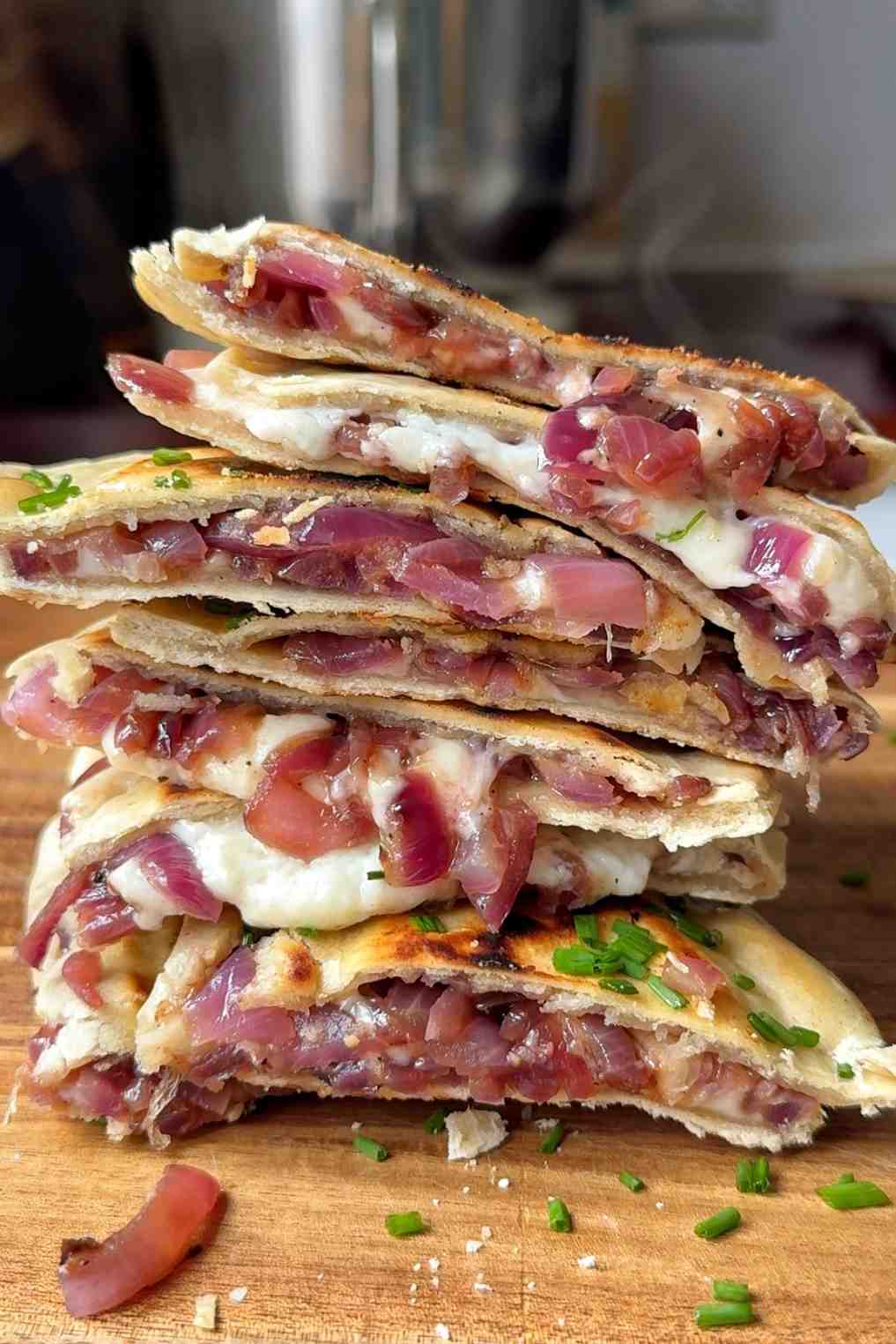 Turkish gözleme stacked and sliced showing caramelized red onion and goat cheese filling on a wooden board.