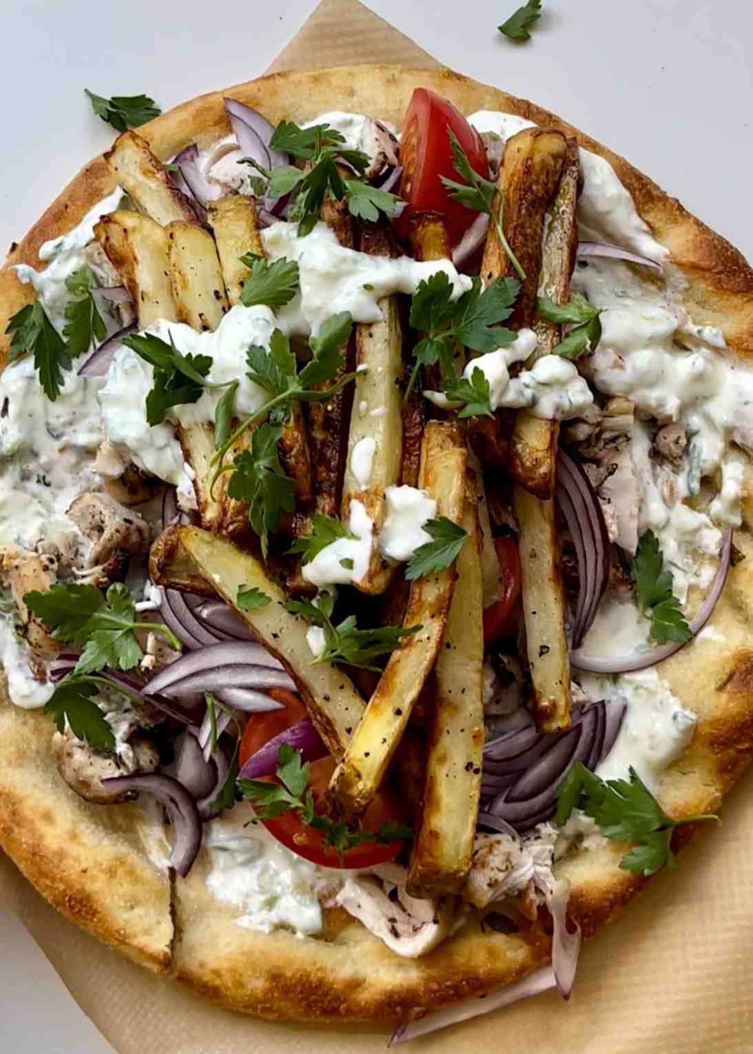 Homemade Greek chicken gyros on a flatbread loaded with air fryer chips tzatziki red onion and tomato.