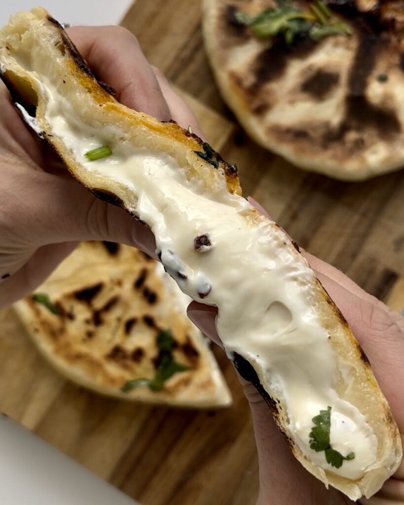 Hands pulling apart a 3-ingredient cheesy naan showing stretchy melted Laughing Cow cheese inside.