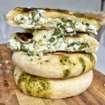 Stacked homemade feta spring flatbreads cut in half showing creamy spinach and feta filling on a wooden board.