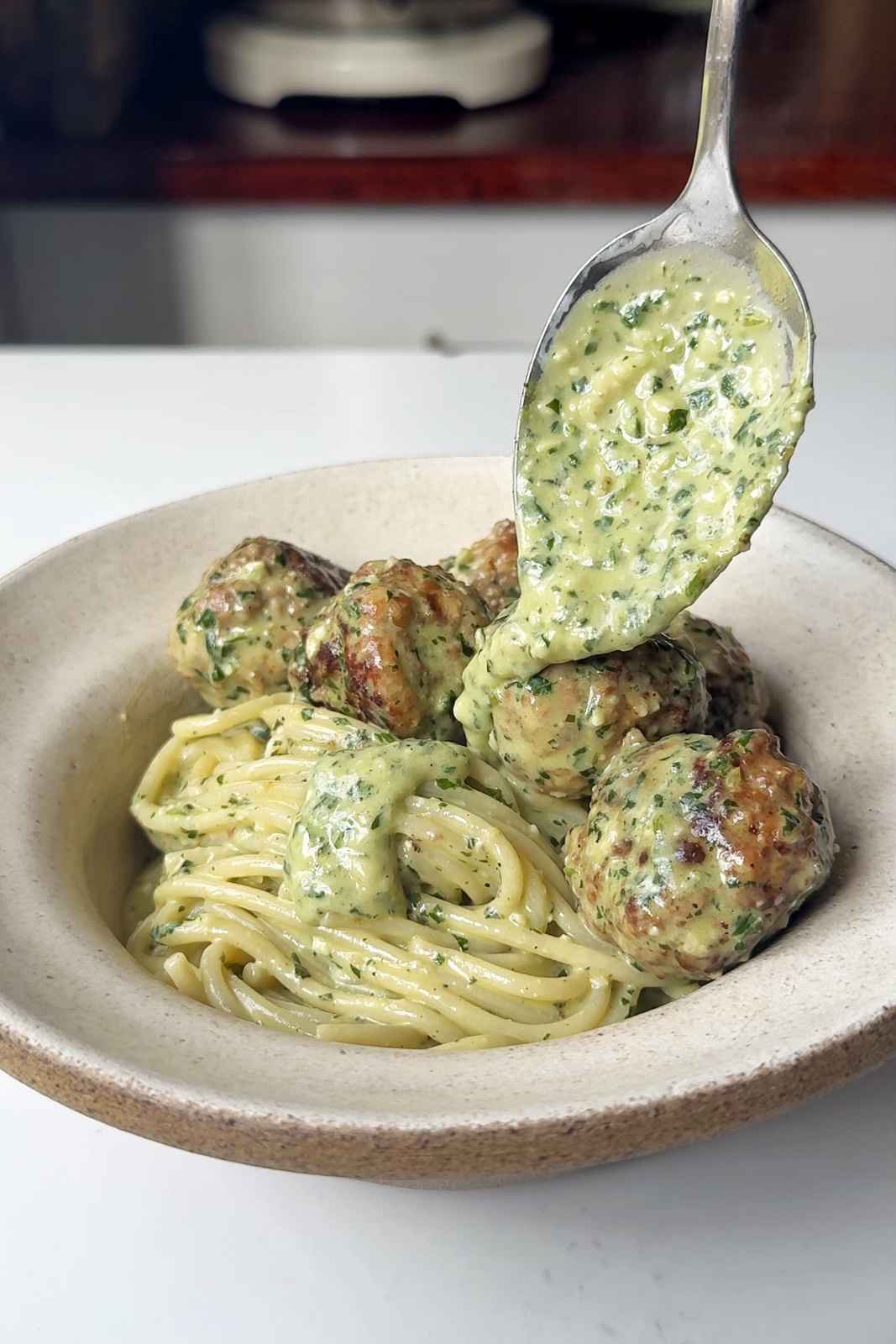 Spooning creamy pesto onto meatballs.