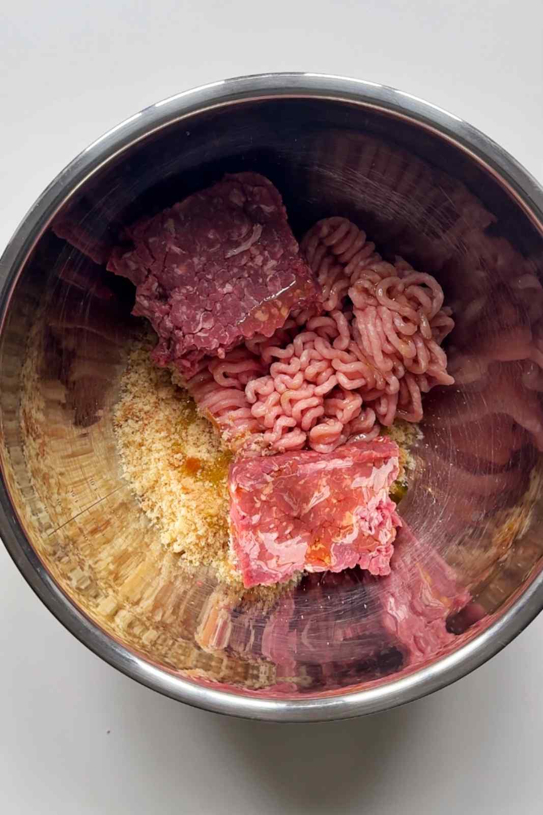 Ground pork and ground beef in a stainless steel bowl to make meatballs.