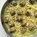 Pesto pasta and meatballs in a stainless steel skillet on a white background.