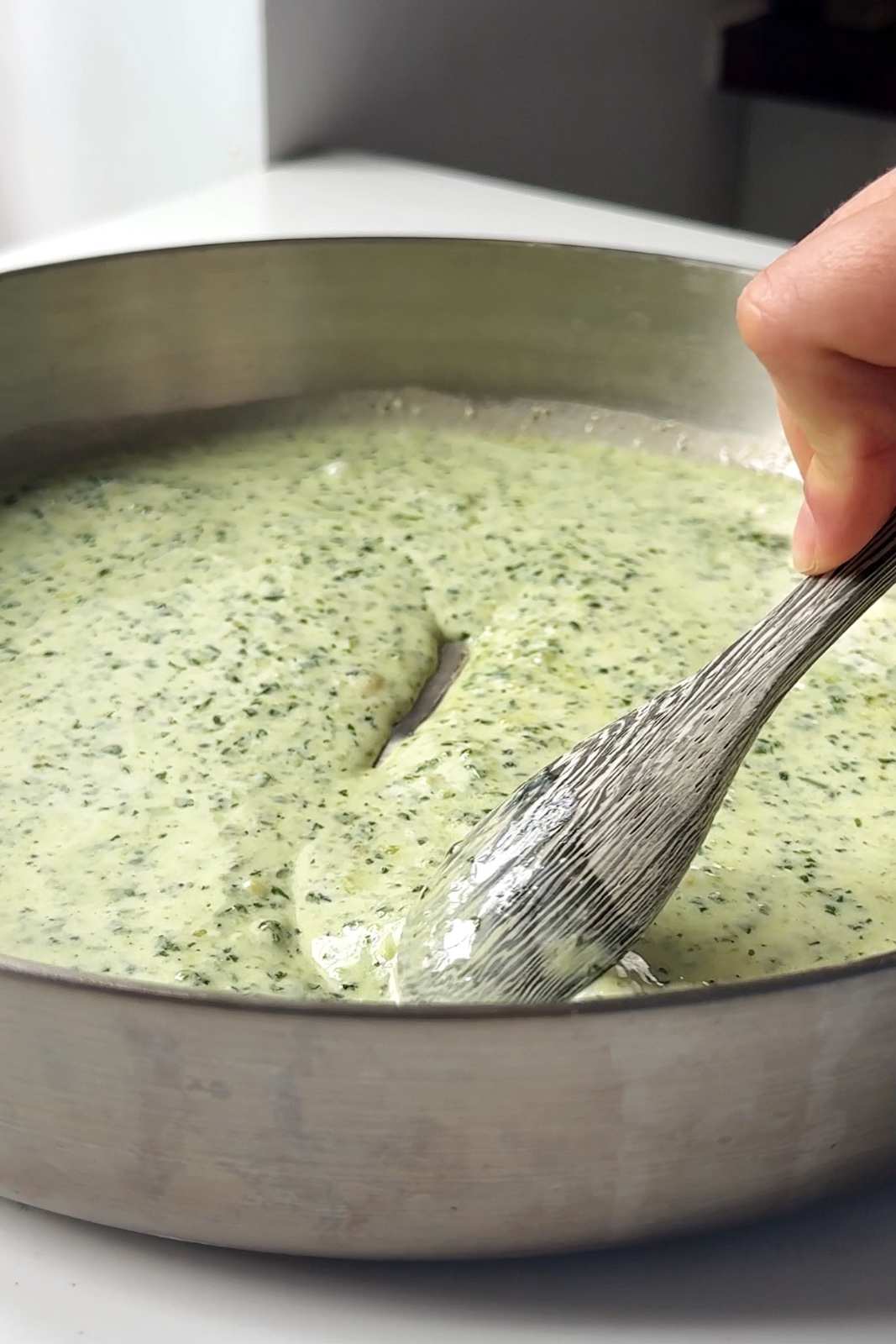 Creamy pesto sauce in stainless steel skillet.