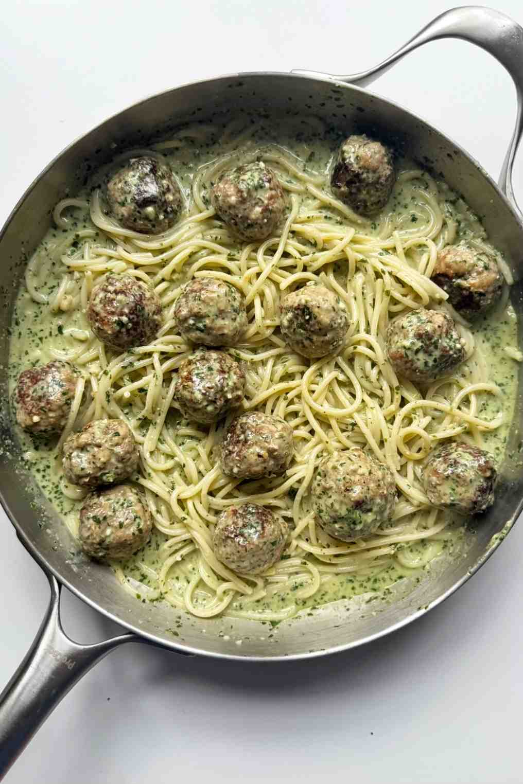 Pesto pasta and meatballs in a stainless steel pan.