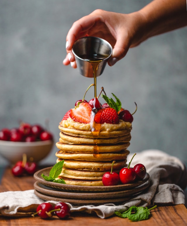 Golden syrup drizzled onto a stack of pancakes with fresh strawberries and cherries — one of many substitutes for maple syrup.