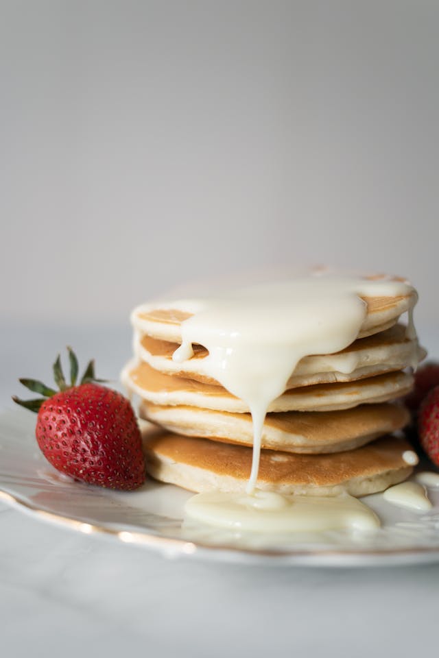 Creamy buttermilk syrup dripping down a stack of pancakes served with fresh strawberries.