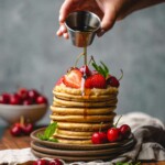 Golden syrup drizzled onto a stack of pancakes with fresh strawberries and cherries — one of many substitutes for maple syrup.