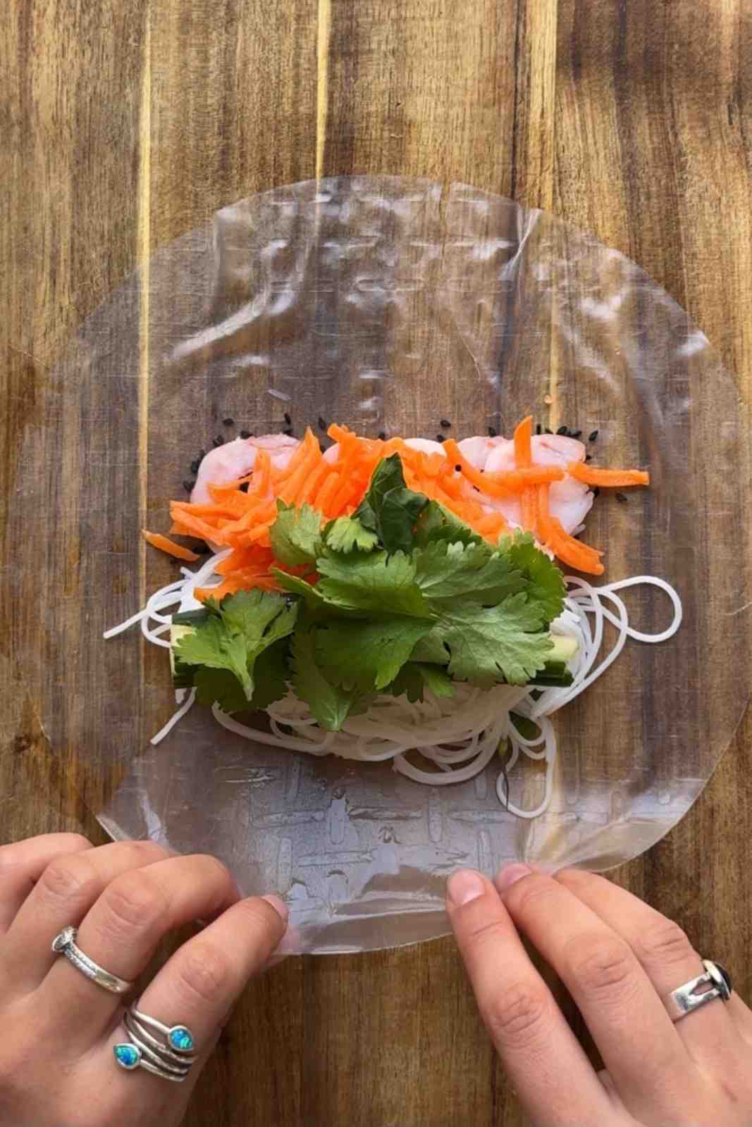 Wrapping summer rolls on a wooden chopping board.