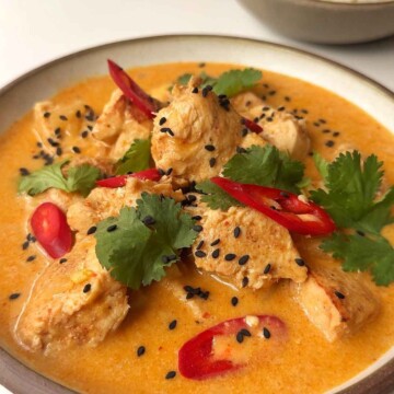 Close up of thai peanut chicken curry in brown bowl topped with red chillies and cilantro.