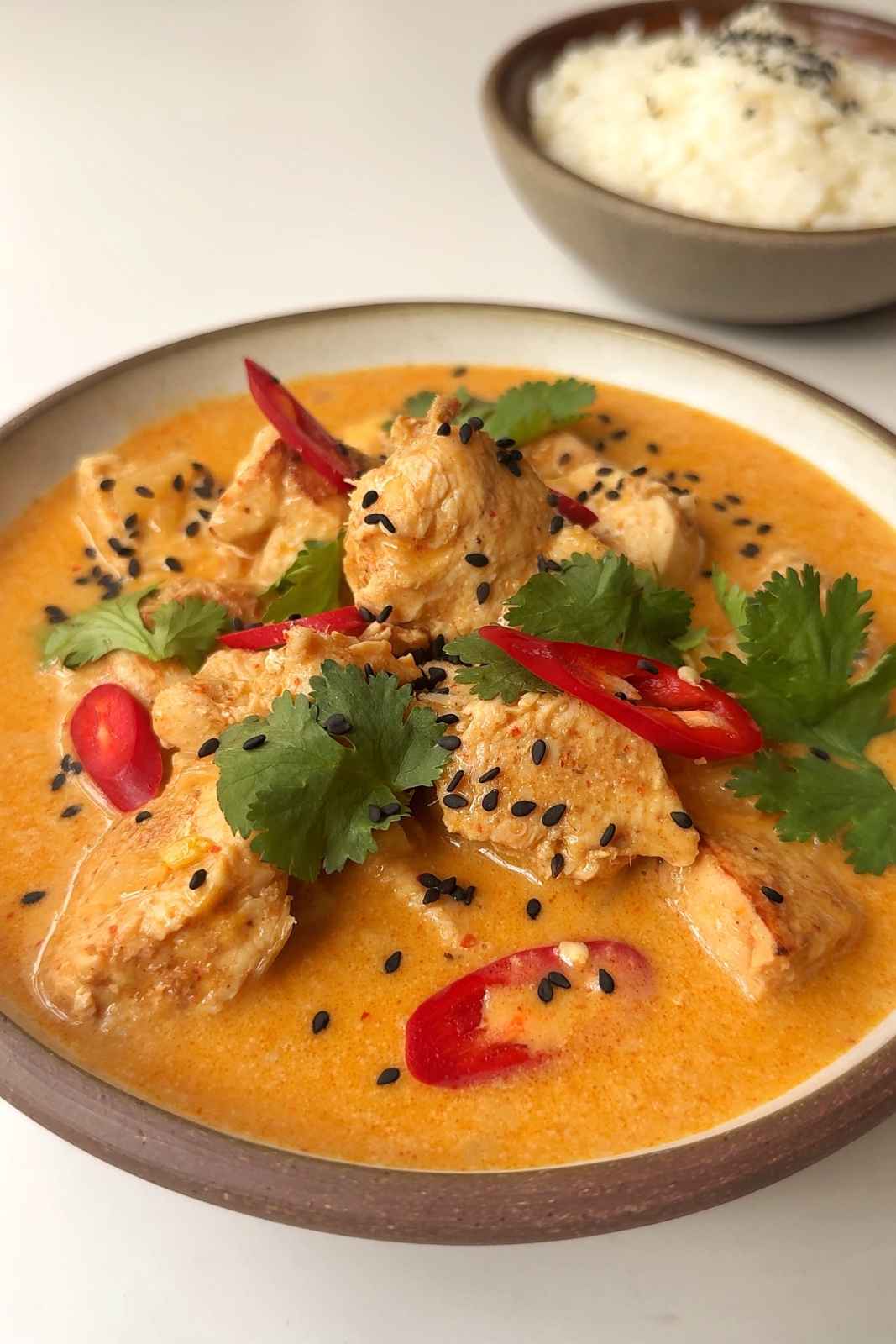Close up of thai peanut chicken curry in brown bowl topped with red chillies and cilantro.