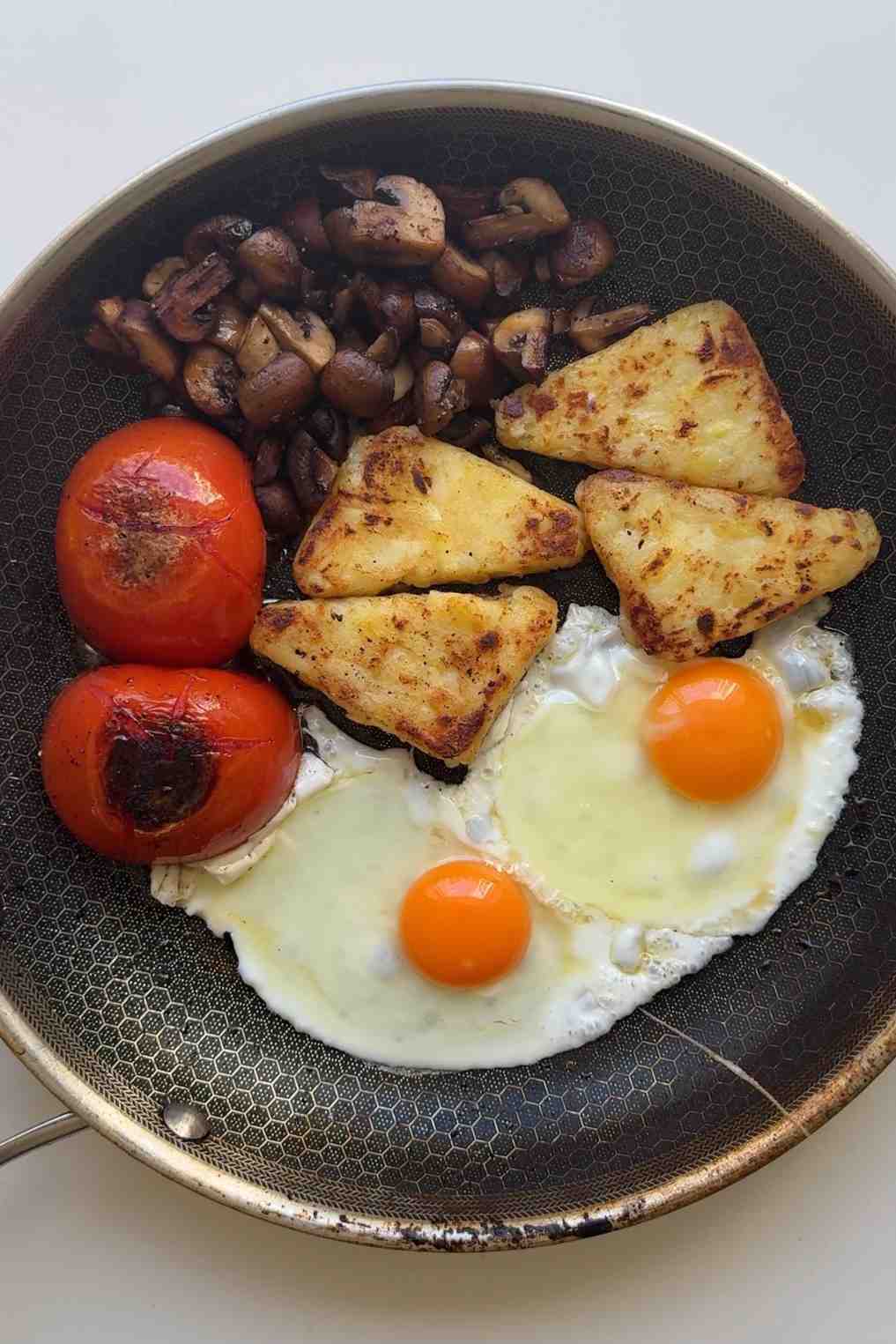 Frying eggs in a pan with tomatoes, hash browns and mushrooms.