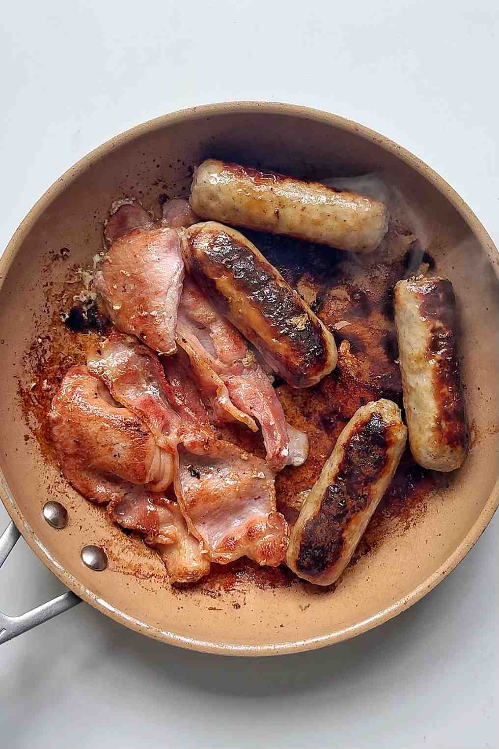 Cooking sausages and bacon in a pan.