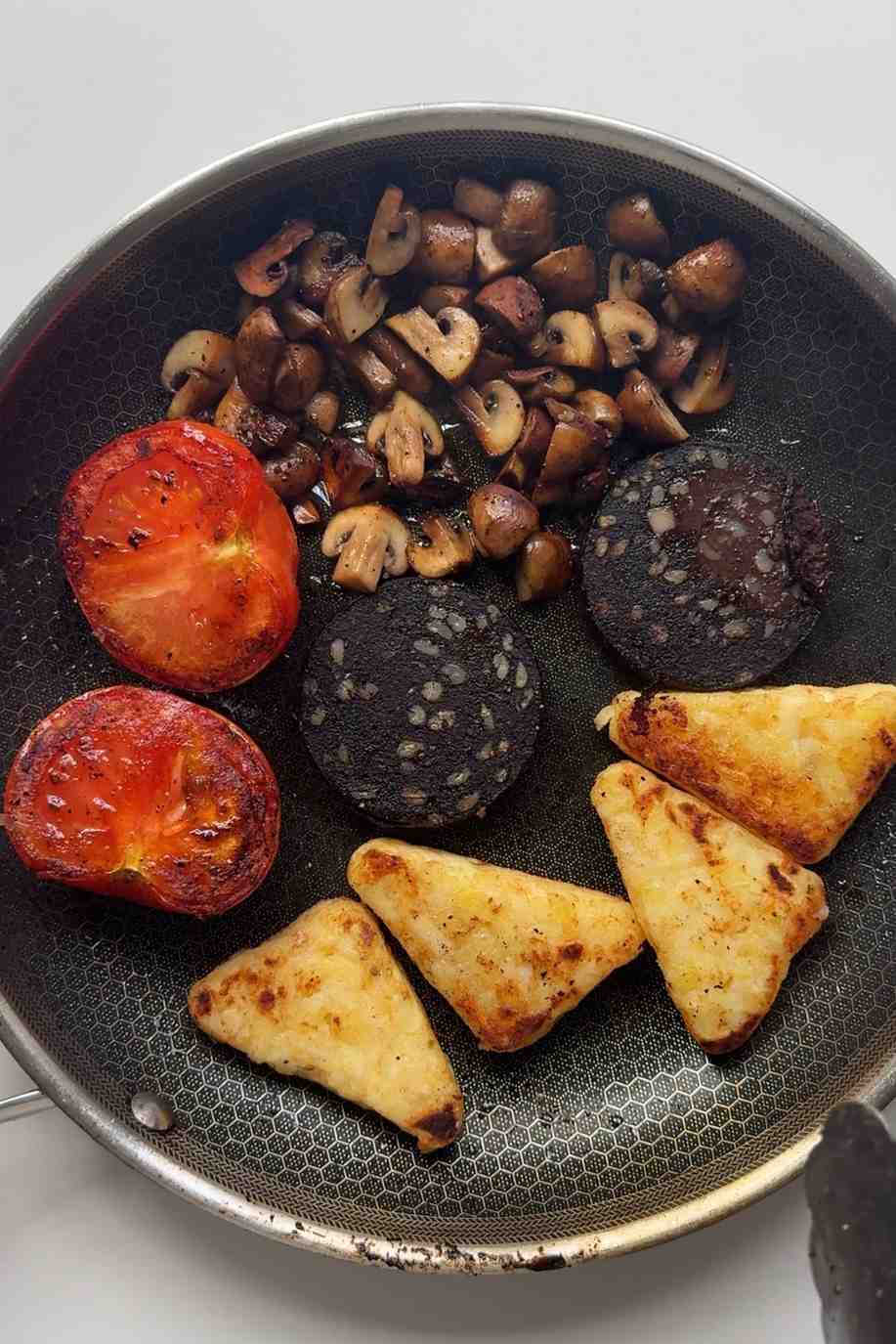 Cooking black pudding and has browns in pan with mushrooms and tomatoes.
