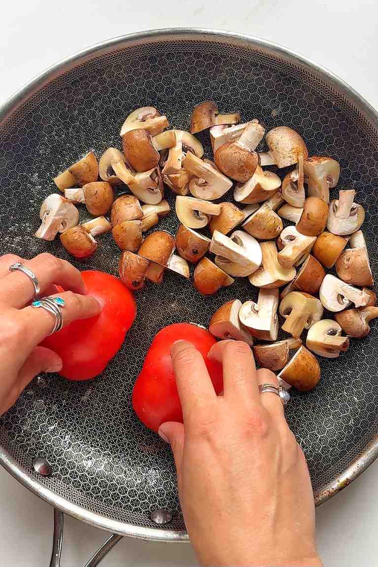 Cooking mushrooms and tomato in a pan.