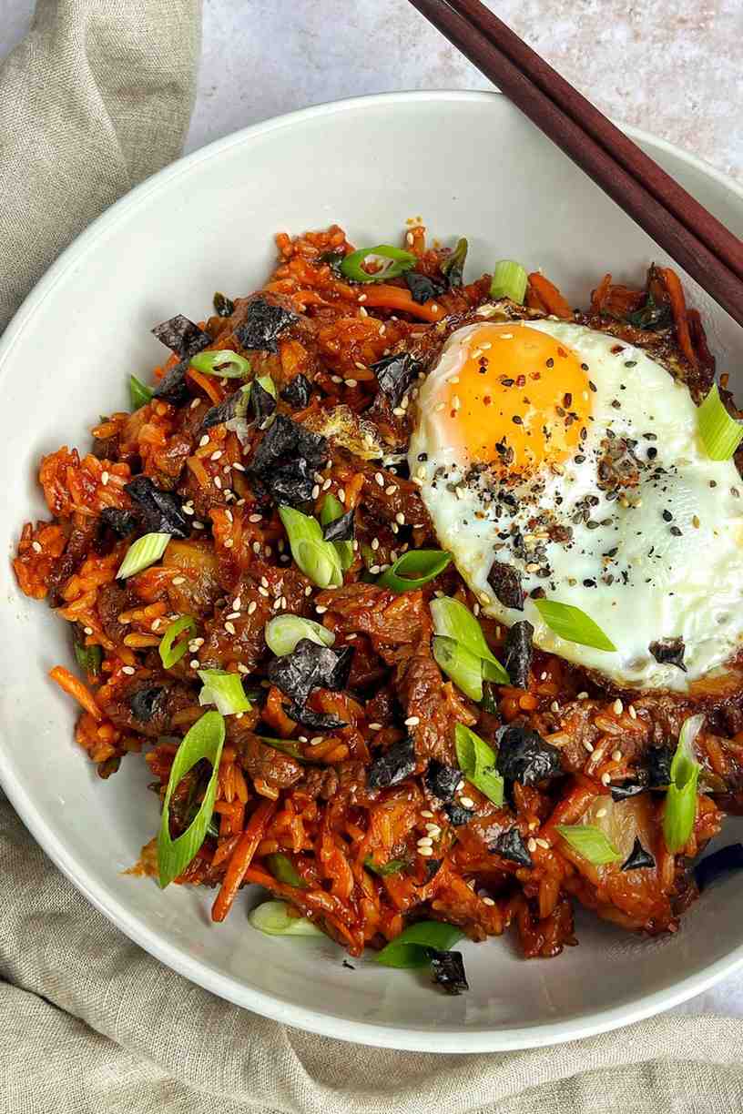 Korean bulgogi fried rice in a white bowl topped with a fried egg, ripped nori sheets, spring onions, and marinated beef on jasmine rice.