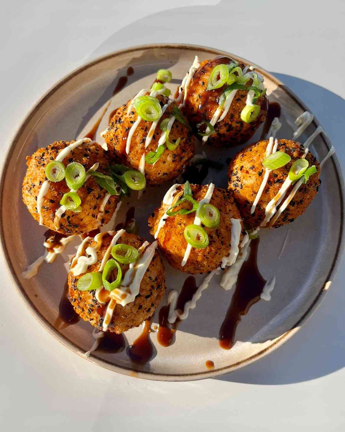 Korean rice balls jumeokbap coated in togarashi and sesame seeds with kimchi tuna mayo filling on a white plate.