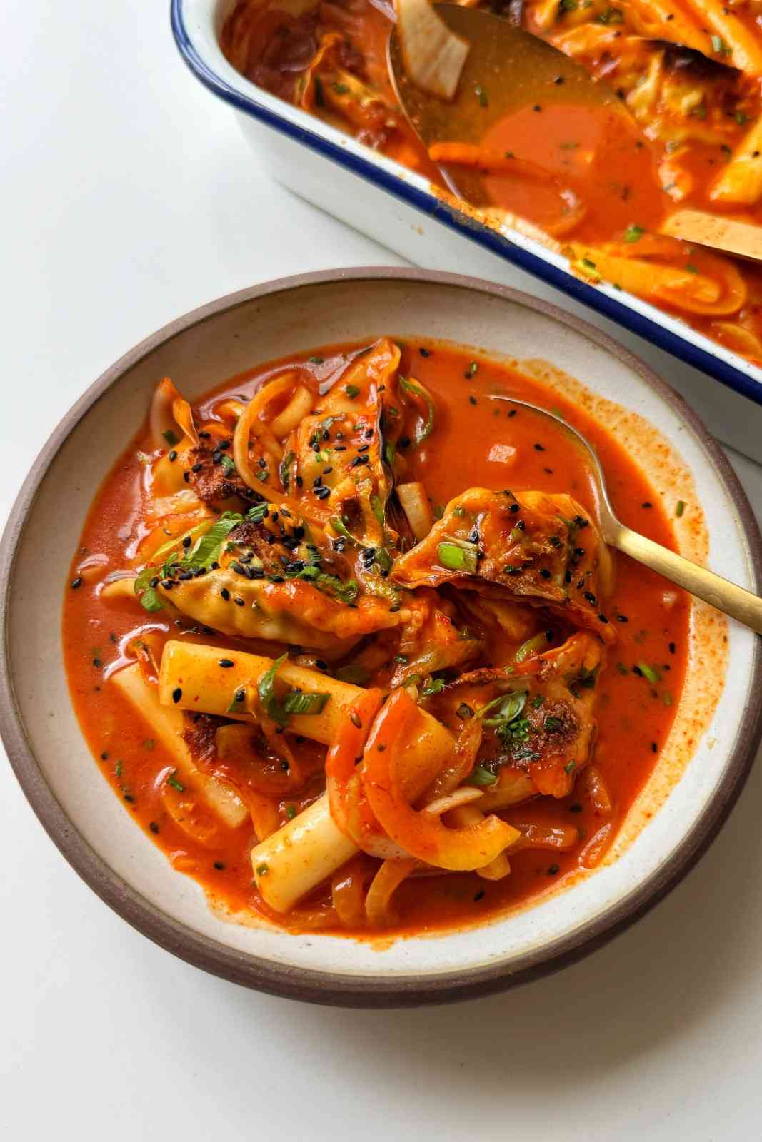 Korean dumpling tteokbokki tray bake with dumplings, rice cakes, mozzarella cheese, and spring onions in a white ceramic bowl.