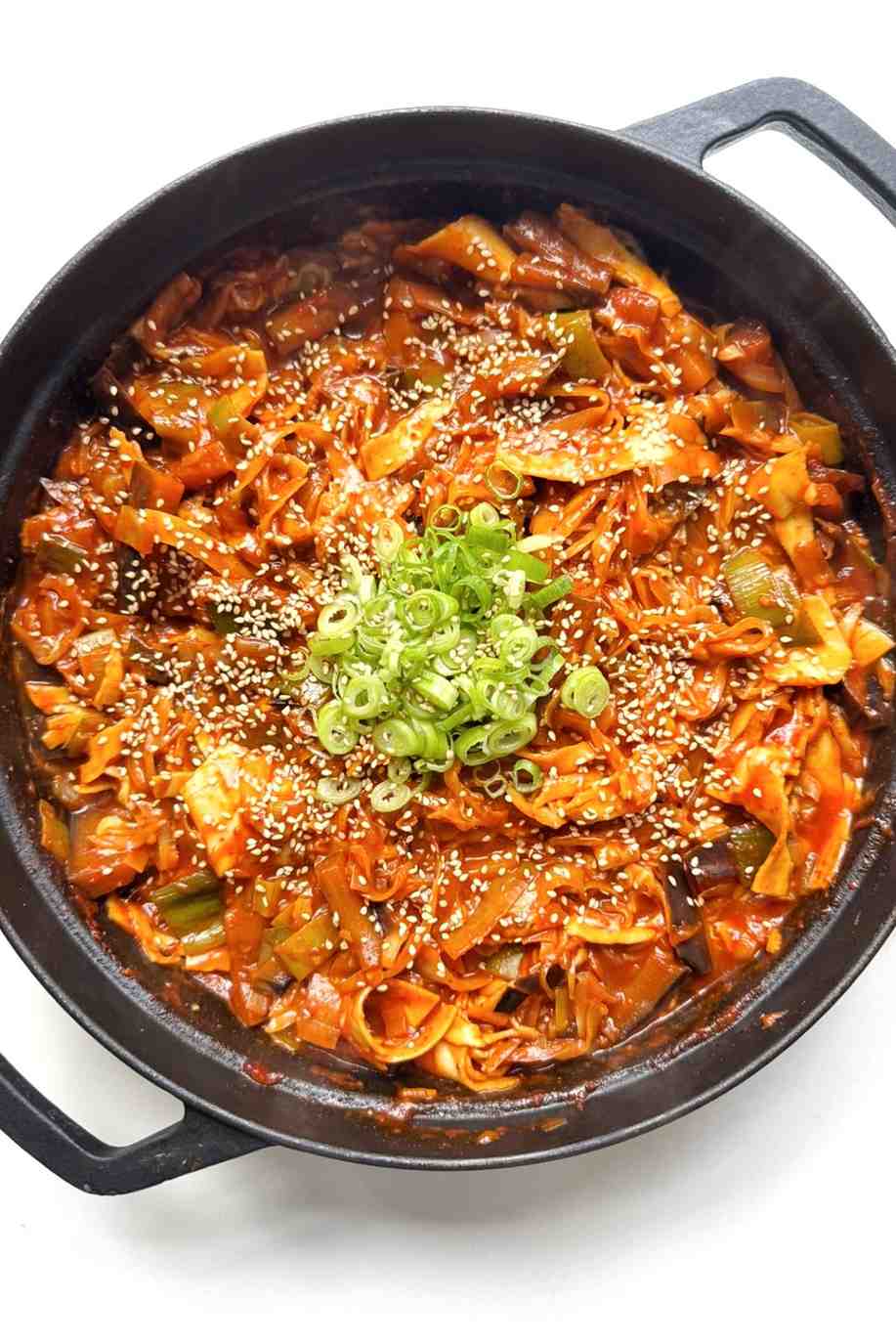 A black pan filled with one pot spicy gochujang lasagne, layered with broken lasagne sheets in a rich red gochujang sauce mixed with white cabbage, sliced leeks, and tender wedges of aubergine, topped with melted mozzarella, sliced spring onions, and toasted sesame seeds.