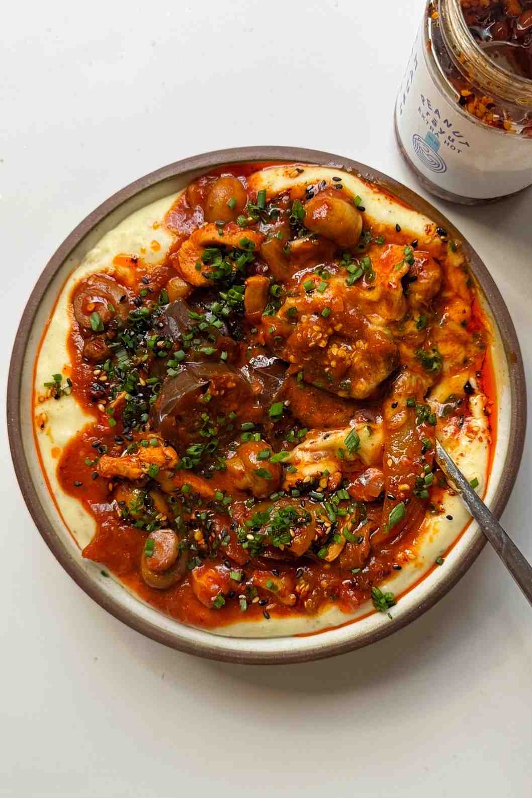 A bowl of Korean-style chicken stew with thinly sliced chicken, silky eggplant, button mushrooms, and kimchi in a glossy red gochujang sauce served over a bed of creamy mashed potato, garnished with chives and a drizzle of chili oil.