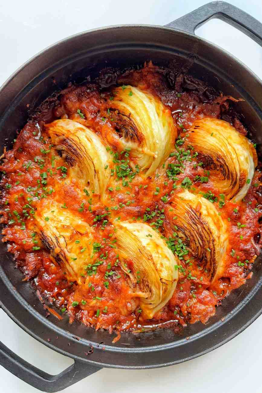 Buldak fire cabbage with charred cabbage wedges in gochujang sauce topped with melted mozzarella in a black cast iron pan.