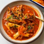 Korean dumpling tteokbokki tray bake with dumplings, rice cakes, mozzarella cheese, and spring onions in a white ceramic bowl.