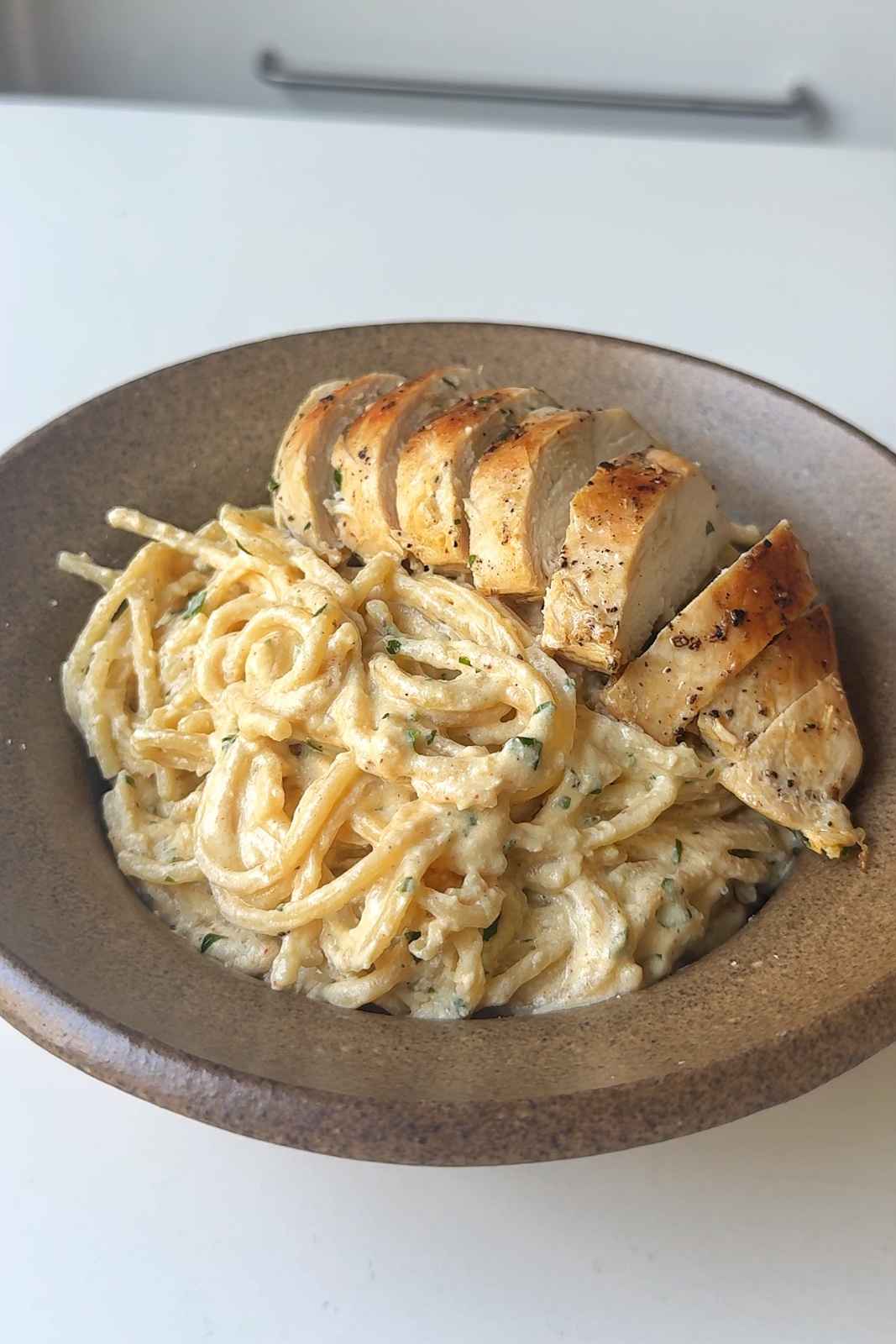 Creamy silken tofu pasta sauce served over spaghetti and topped with fried chicken breast and parsley in a brown bowl, a high-protein silken tofu recipe.
