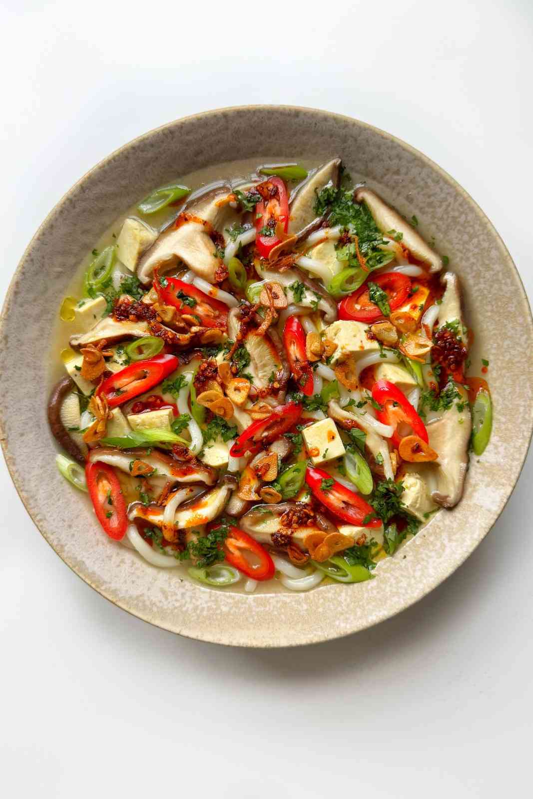 White bowl of easy miso soup with shiitake mushrooms, silken tofu, scallions, red chili, cilantro and homemade garlic ginger oil, a 10-minute silken tofu soup.