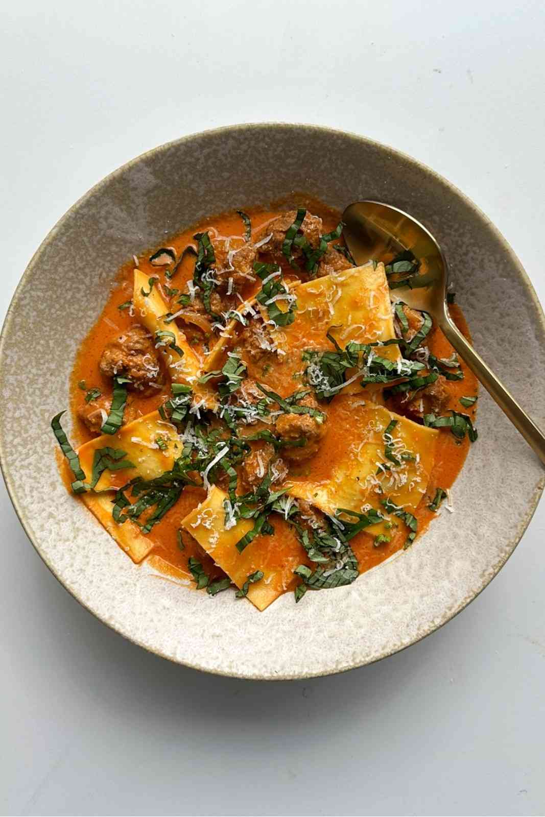 Overhead bowl of deconstructed ravioli soup with lasagna sheet pieces and Italian meatballs in a creamy tomato broth, topped with grated parmesan and fresh basil.