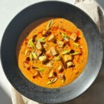 Overhead bowl of creamy tofu tomato soup topped with crispy tofu cubes, sliced scallions, chili oil, and black sesame seeds.