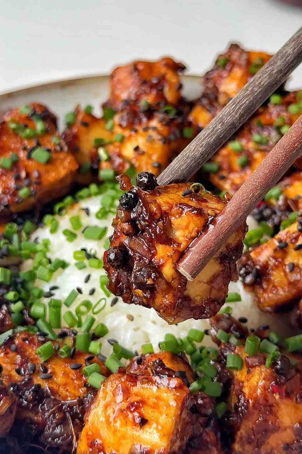 Black pepper tofu being held up to the camera with a chopstick.