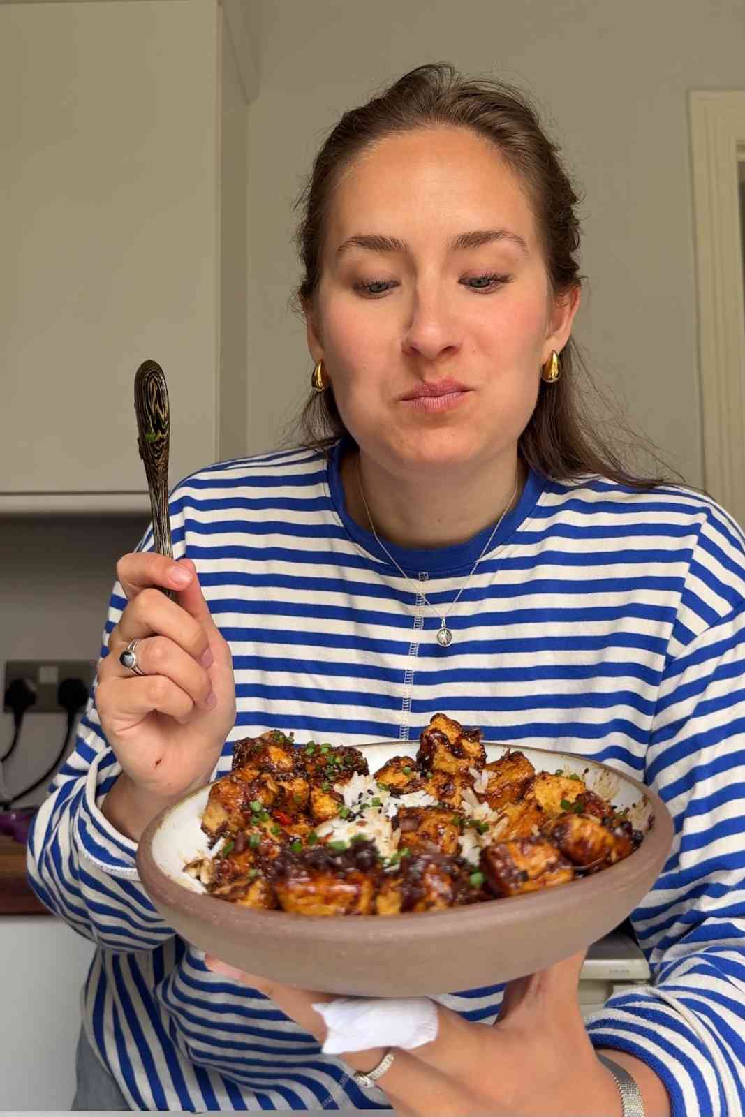 Emily eating black pepper tofu with a white and blue stripe top.