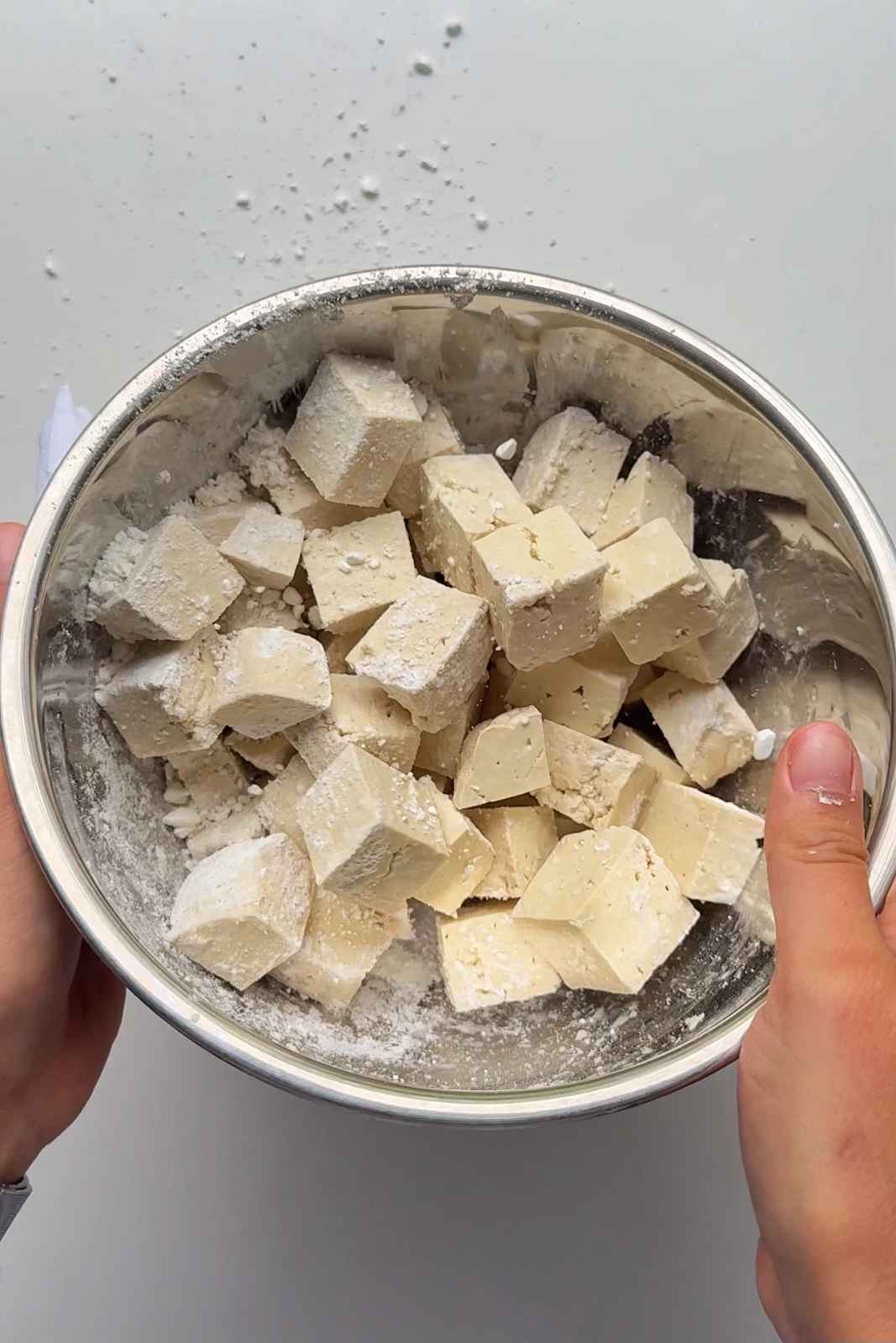 tossing tofu in cornflour in a stainless steel bowl.
